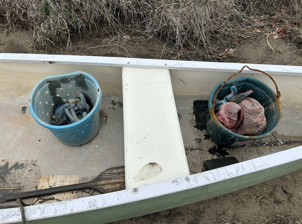 Two buckets sit inside of a canoe sitting on land. 